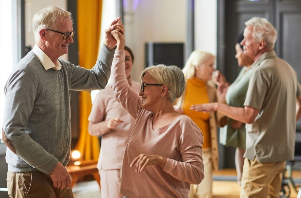 A group of older adults dance together in their community home.
