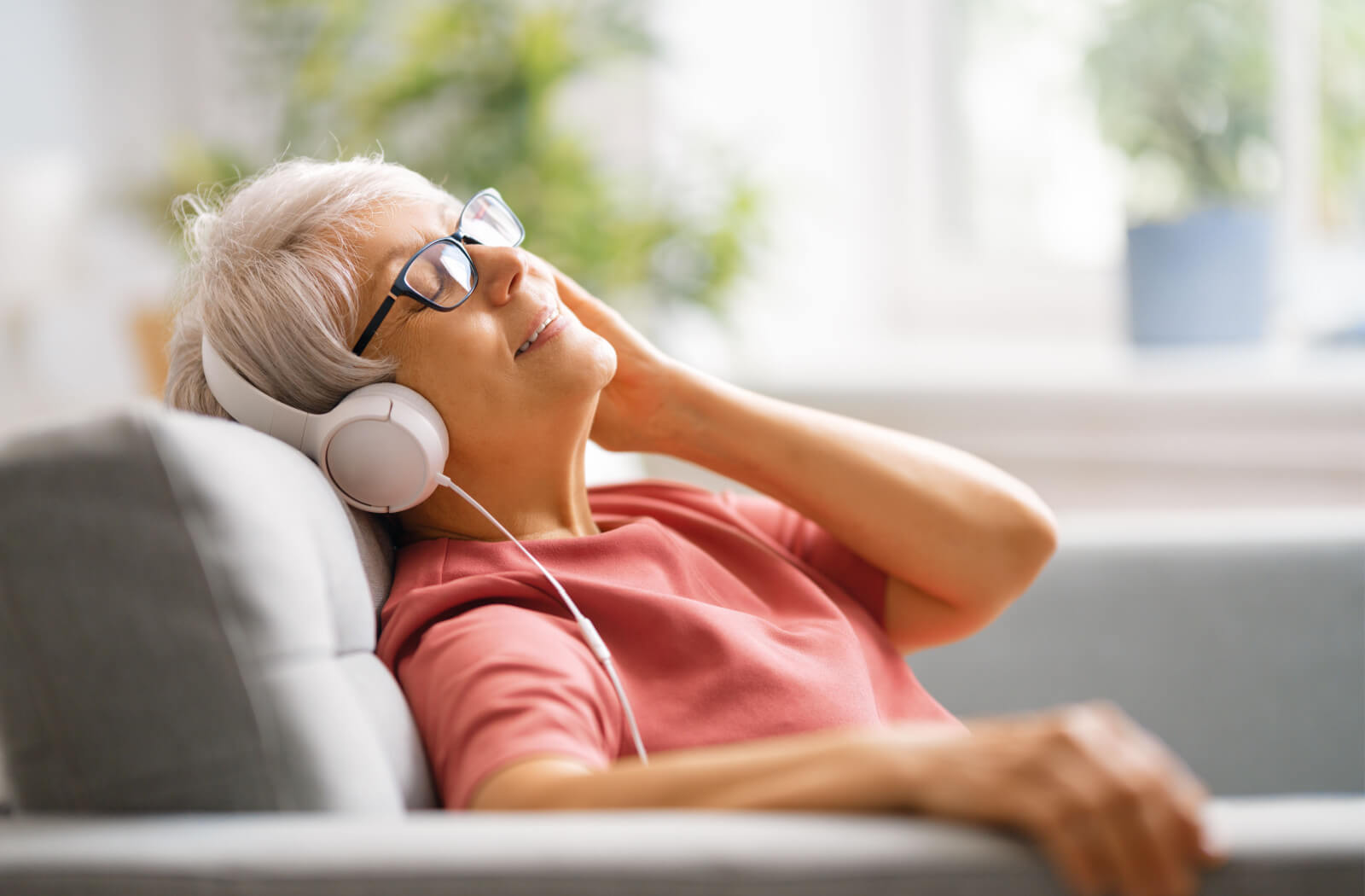 A senior woman leaning back on her couch as she listens to music.
