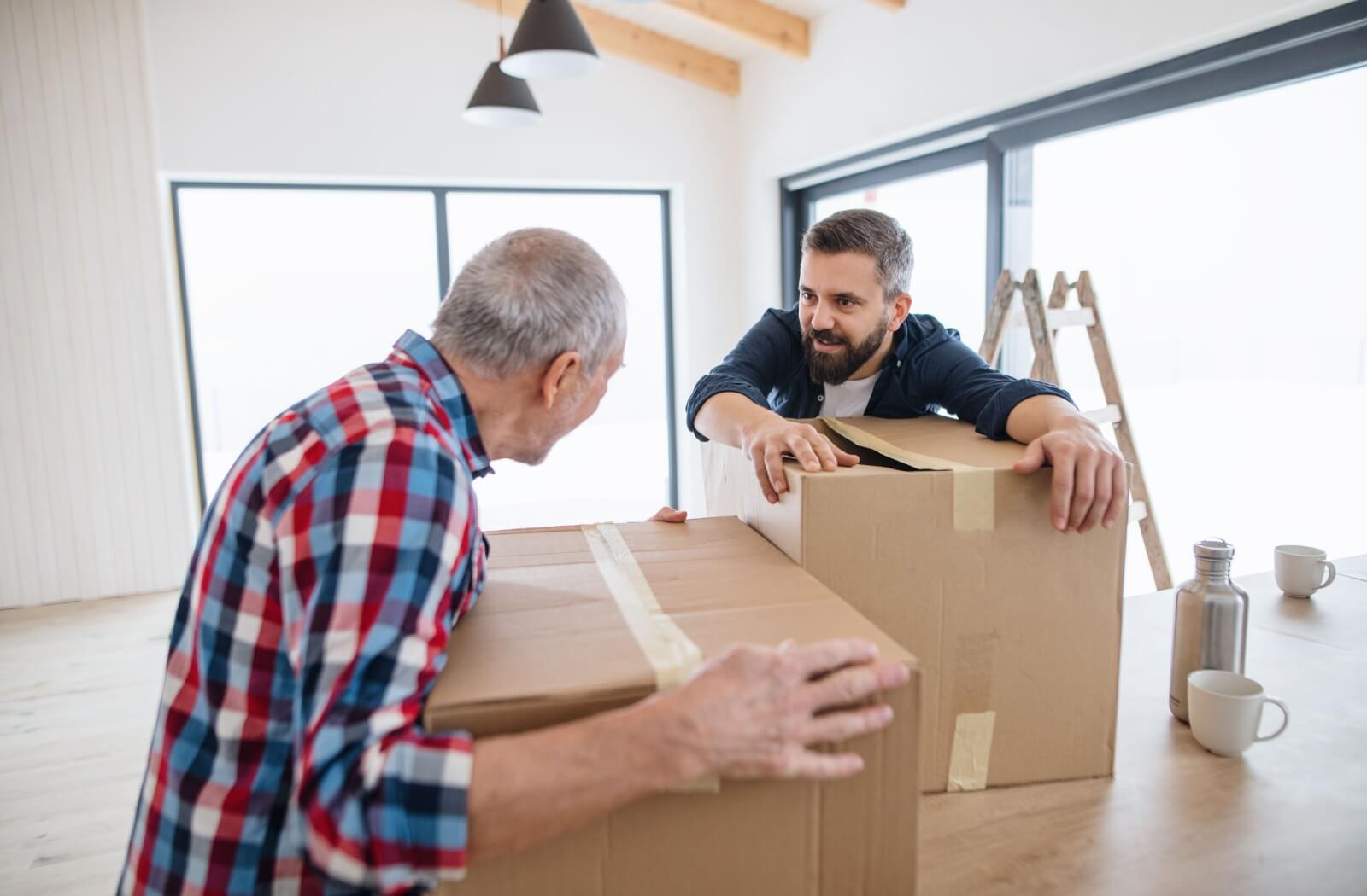 Adult son helping his father pack moving boxes in a bright home, preparing for a transition to memory care.